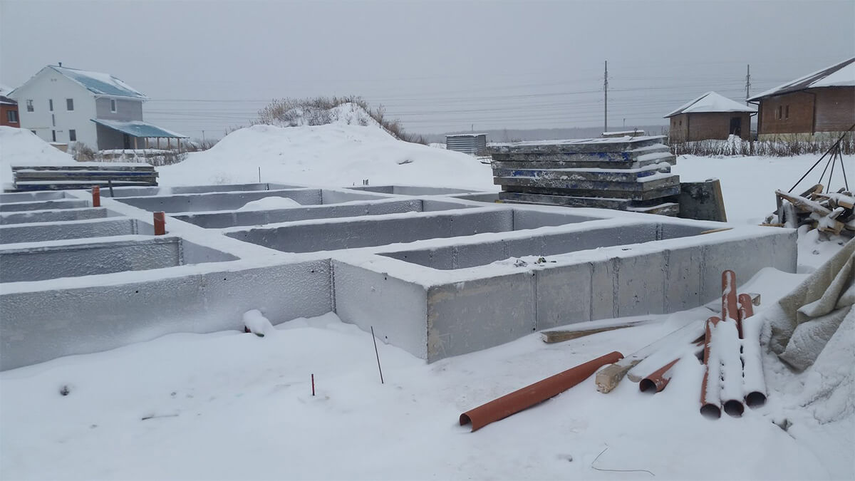Рабочие укладывают фундамент на заснеженной площадке
